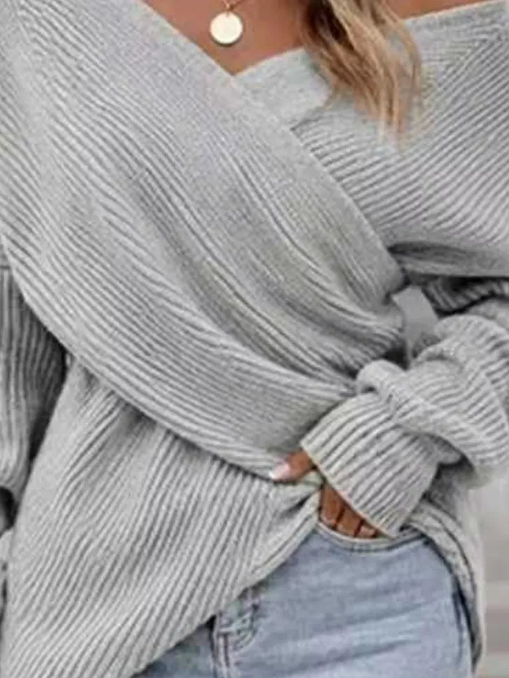 A close-up of a person wearing a light gray ribbed knit off-the-shoulder sweater tied at the waist, paired with light blue jeans.